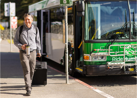 Man walking beside a bus that just dropped him off at the airport on a nice sunny day.