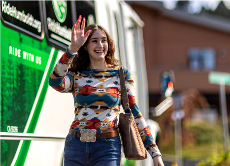 Picture of a college-age woman walking beside a bus and waving